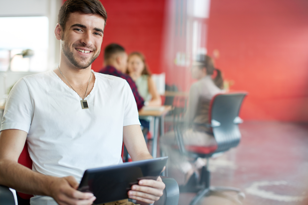 Confident male designer working on a digital tablet in red creative office space